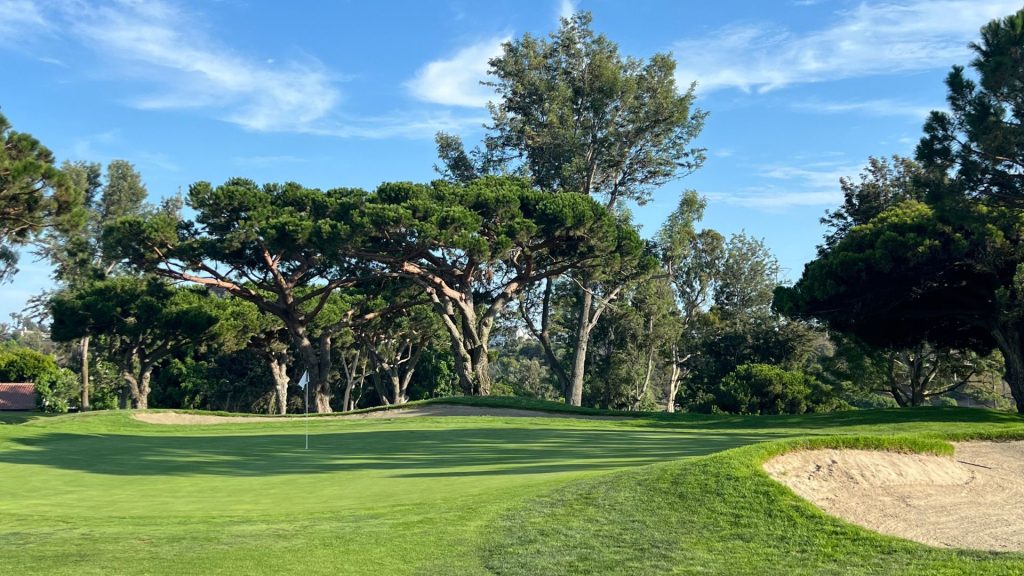 Putting green with a white flag guarded by sand bunkers and framed by mature pine trees at Lomas Santa Fe Executive Golf Course